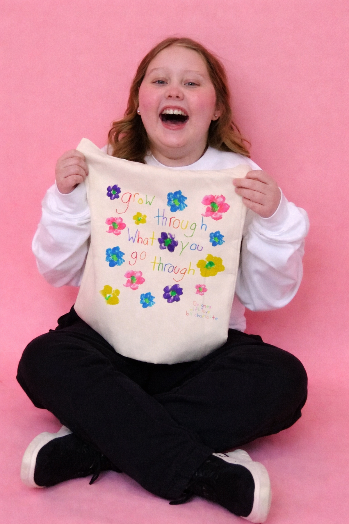 Charlotte smiling and holding her flower-print Grow Through What You Go Through tote bag